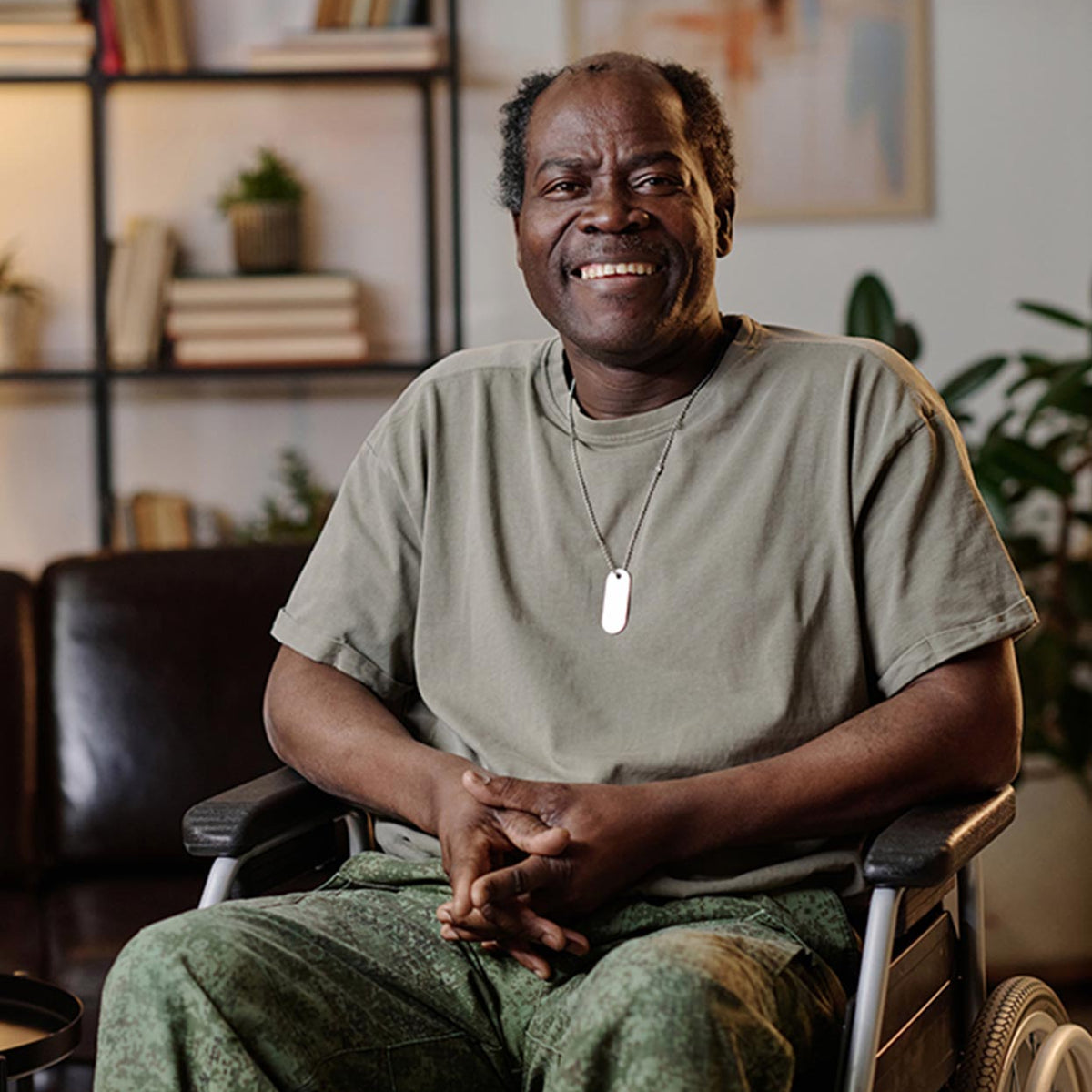 Man sitting in a wheelchair in a home setting with bookshelves and plants.