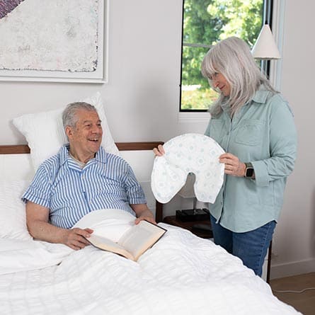 Woman showing a QuickChange Wrap to a man in bed, with a book on the bed.