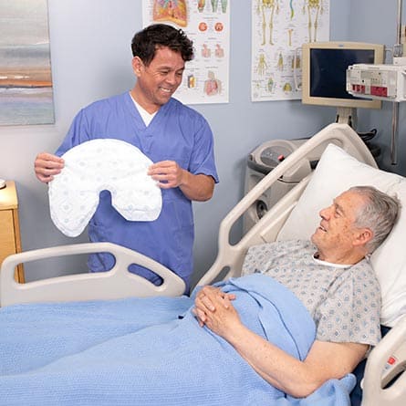 Man in blue scrubs holding a Quick Change Wrap to a patient in a hospital bed.