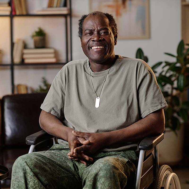 Man in a wheelchair smiling in a home setting with books and plants.